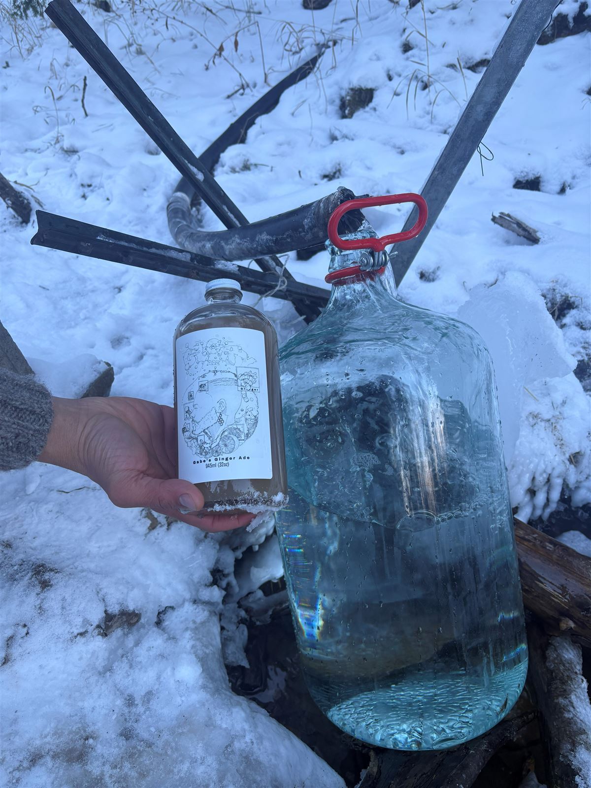Gabe's Ginger Ade beside a jug of fresh spring water in winter